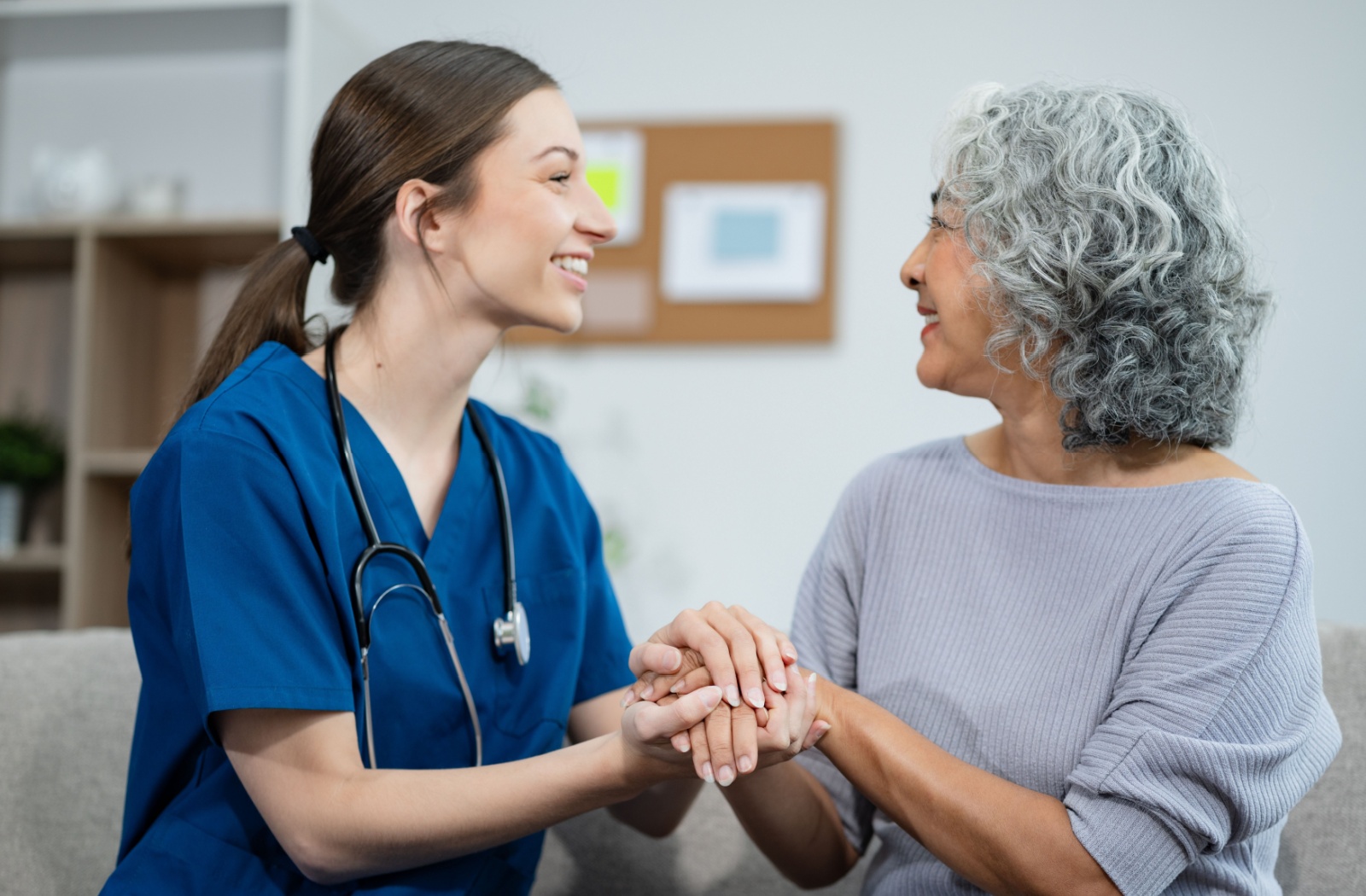 A caregiver and resident in memory care clasping hands and smiling at one another.
