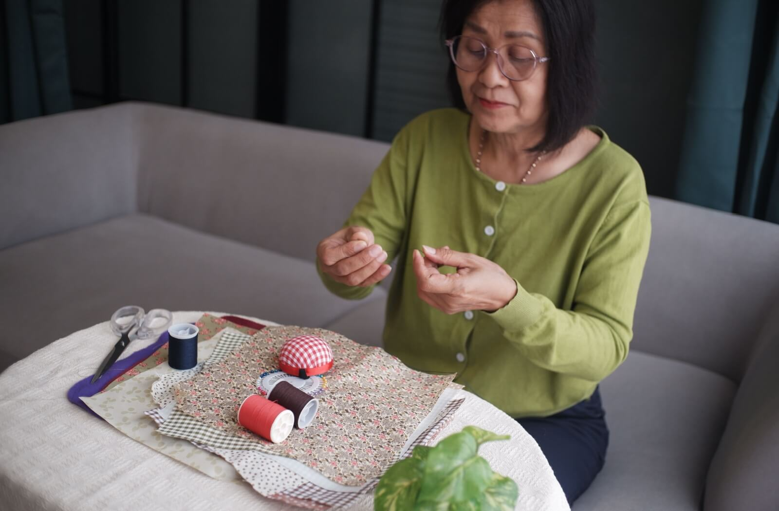 Senior threading a needle at a table with fabric scissors and colorful spools of thread for quilting
