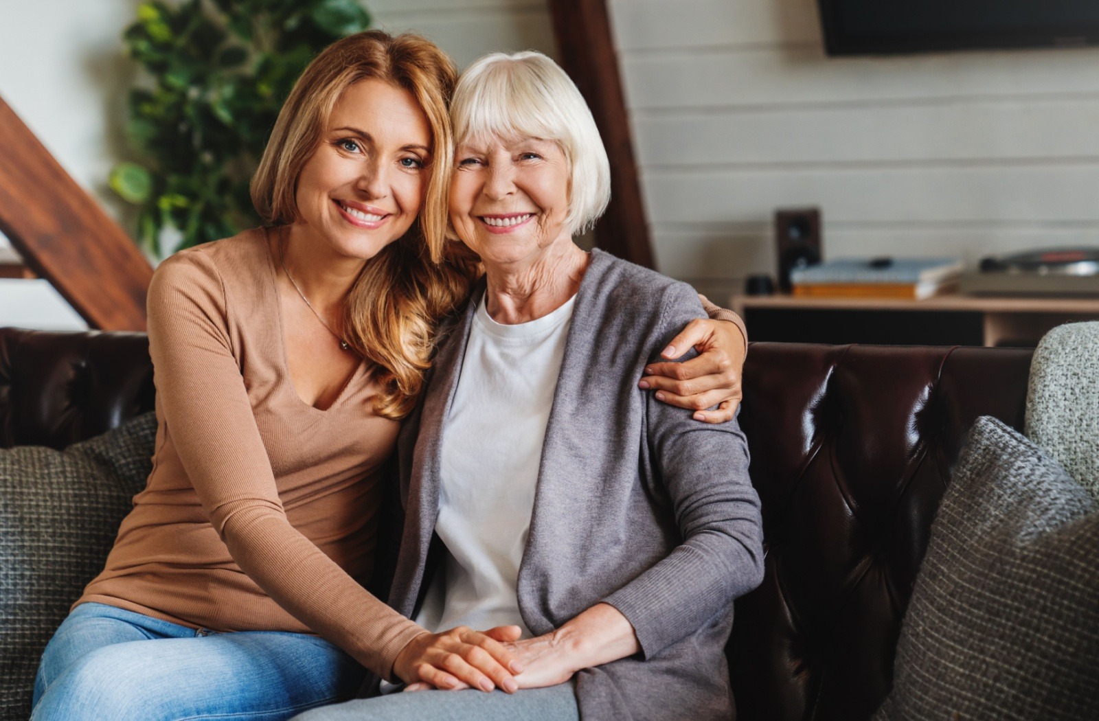 An adult child embraces their senior parent while sitting on a couch.
