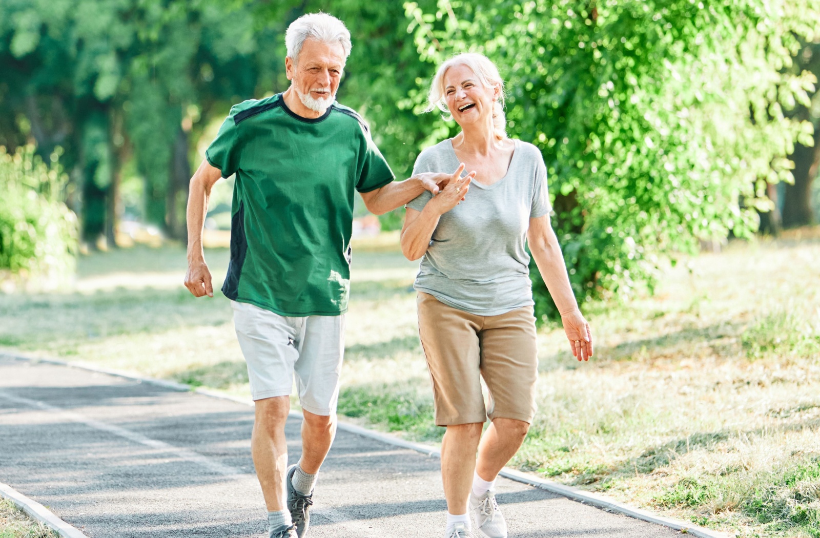 Two older adults laugh while walking together along a trail in a park