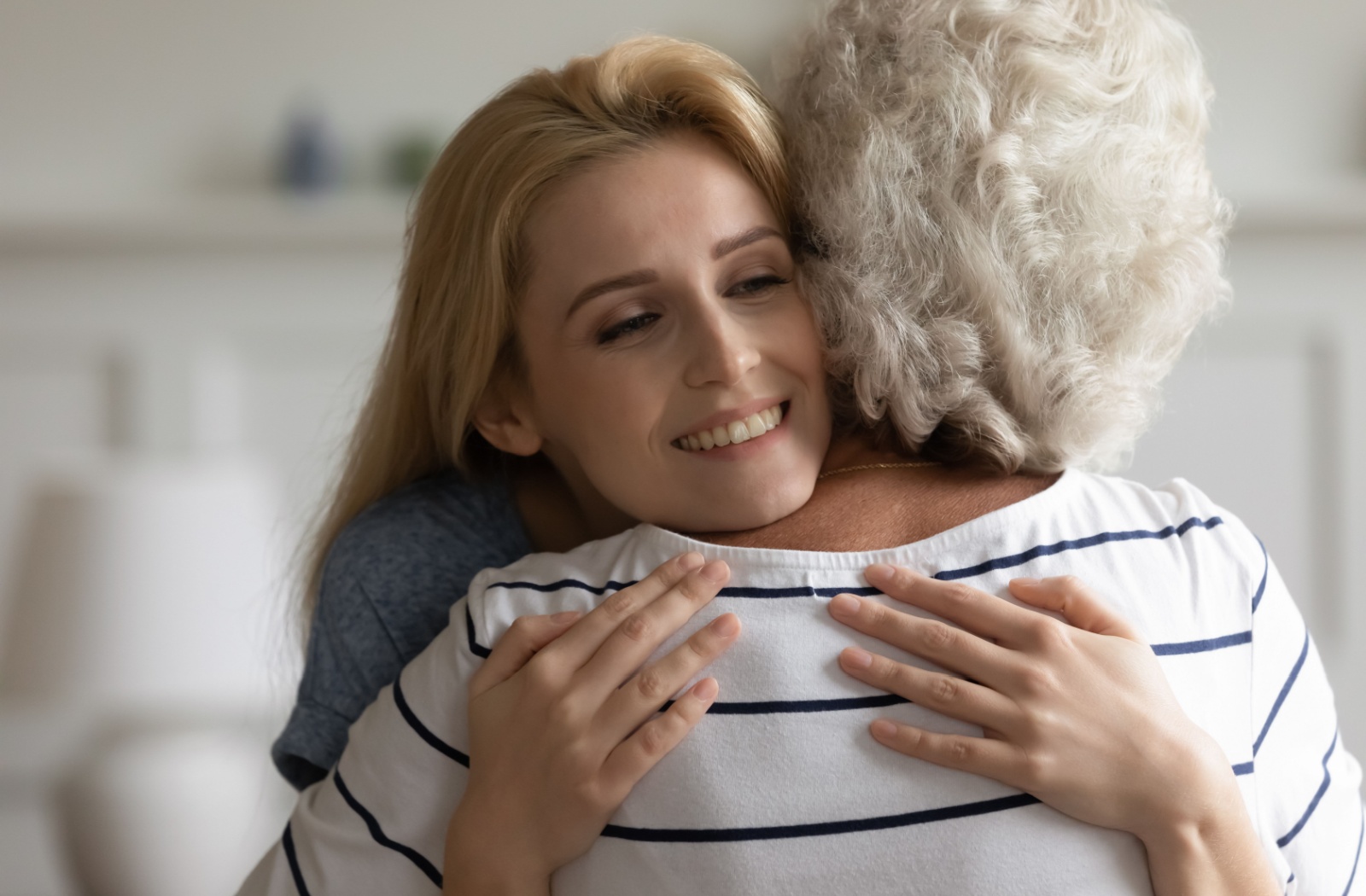 Smiling adult hugs her aging mother.