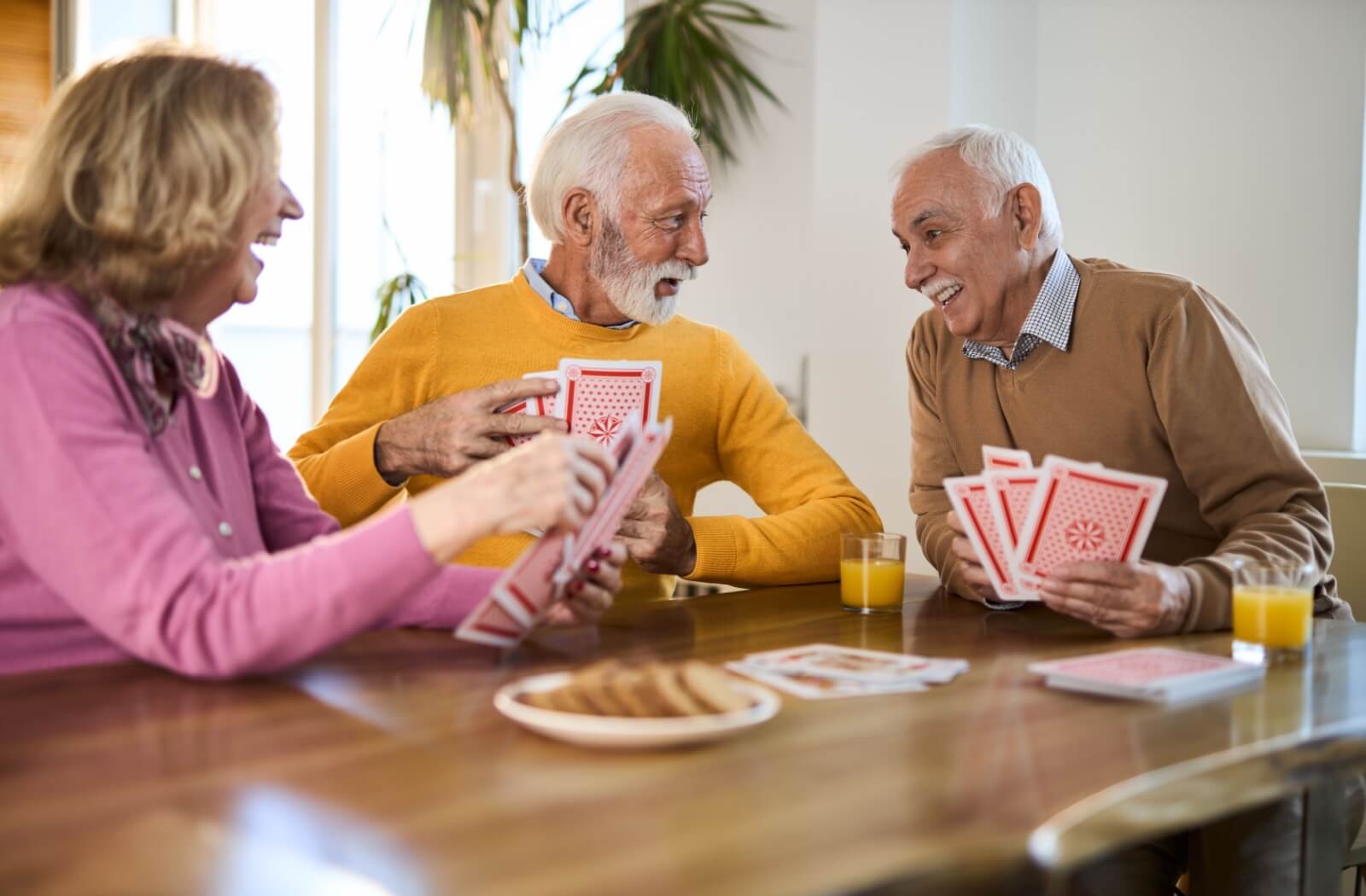 A smiling group of older adults sitting at a table and playing cards.
