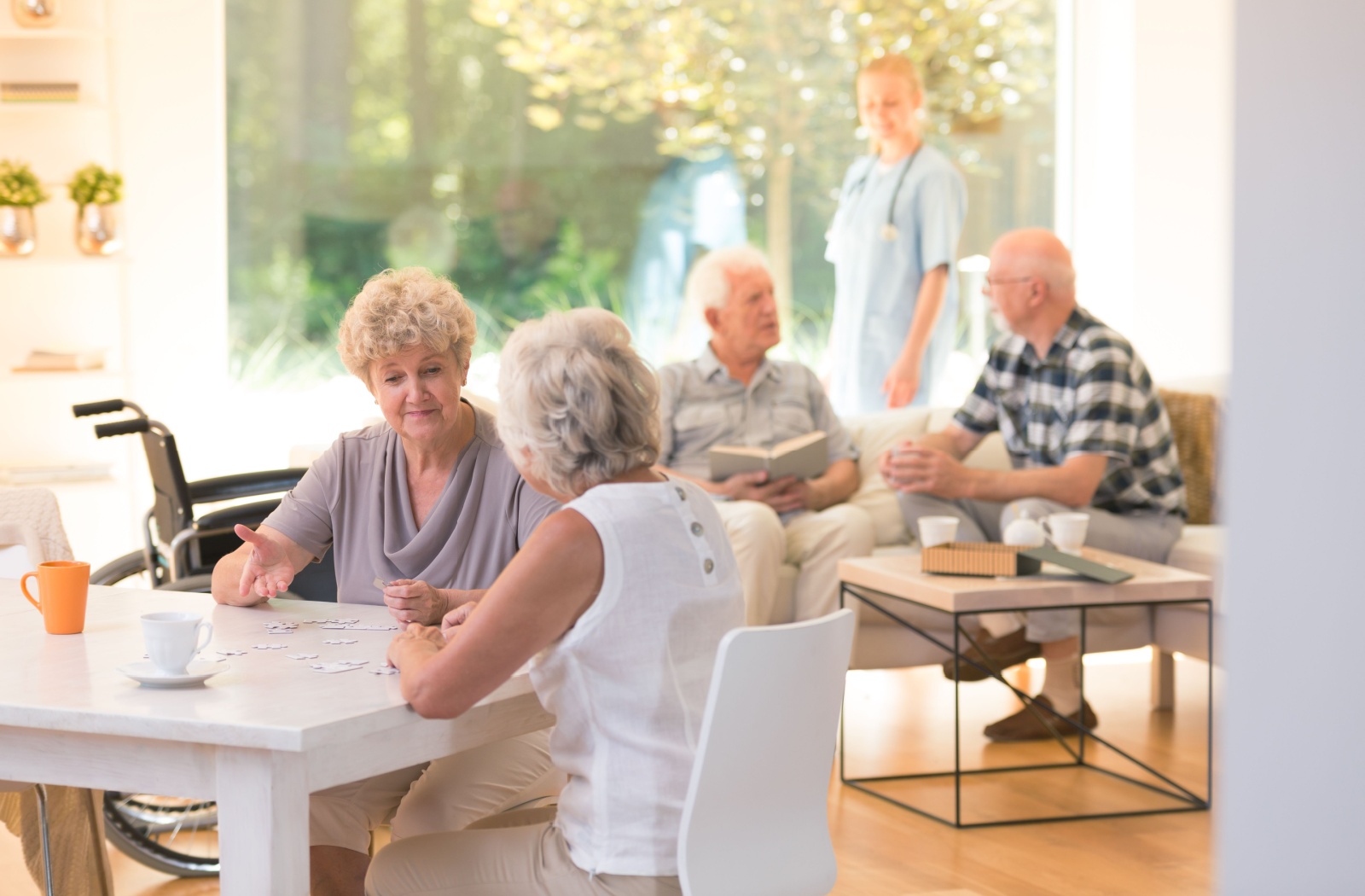 Older adults socializing in a common room in a retirement community with a staff member standing in the background.
