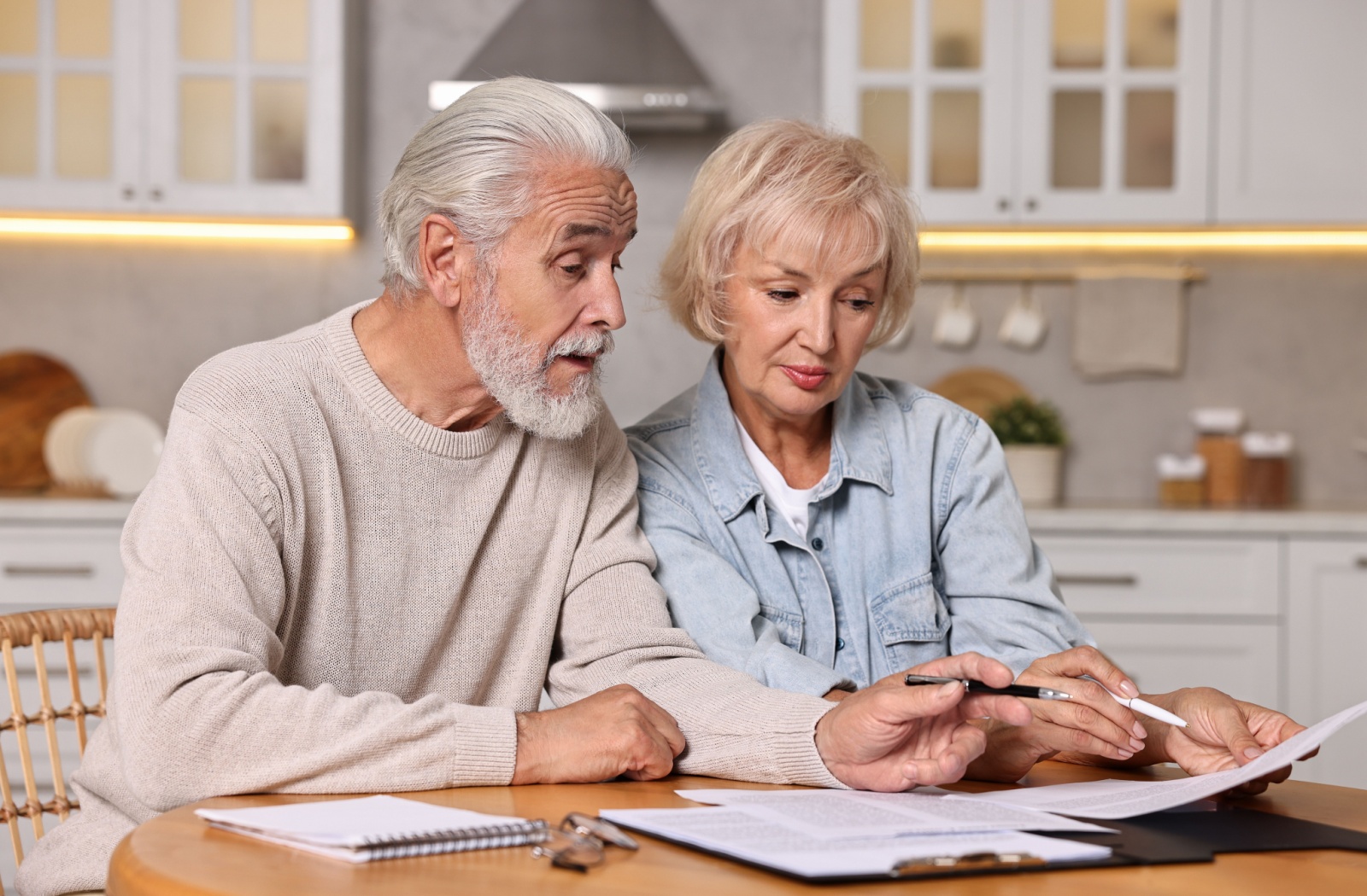 An older couple sitting at a desk and looking at paperwork.